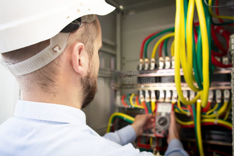 Serviceman adjusts fuse box. Electrician engineer measures voltage in a power electrical cabinet royalty free stock photography