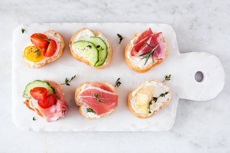Servierplatte von Frischkäse crostini Aperitifs mit einer Mischung von Belägen über einem weißen Marmorhintergrund lizenzfreie stockfotos