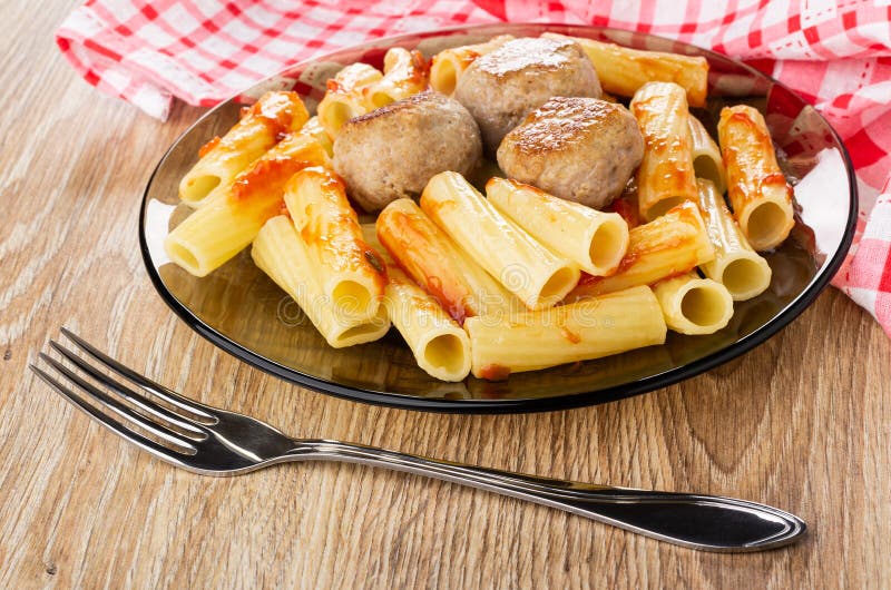 Serviette, pâtes cuites avec des boulettes de viande, ketchup dans le plat brun, fourchette sur la table en bois photo libre de droits Serviette, pâtes cuites avec des boulettes de viande, ketchup dans le plat brun, fourchette sur la table en bois photo libre de droits
