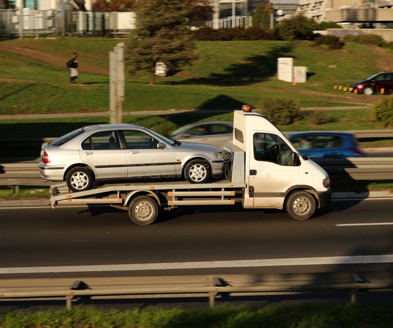 Silver car, being towed, on a towing truck speeding on a highway. Silver car, being towed, on a towing truck speeding on a highway