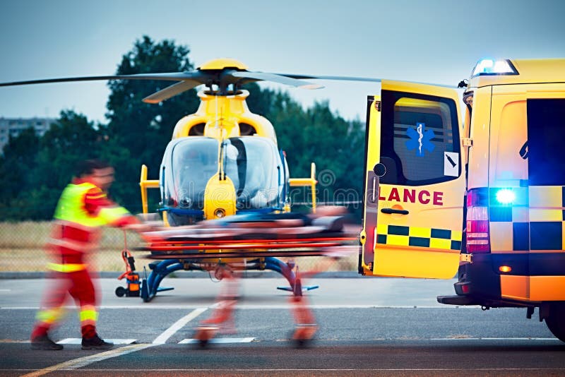 Cooperation between air rescue service and emergency medical service on the ground. Paramedic is pulling stretcher with patient to the ambulance car. Cooperation between air rescue service and emergency medical service on the ground. Paramedic is pulling stretcher with patient to the ambulance car.