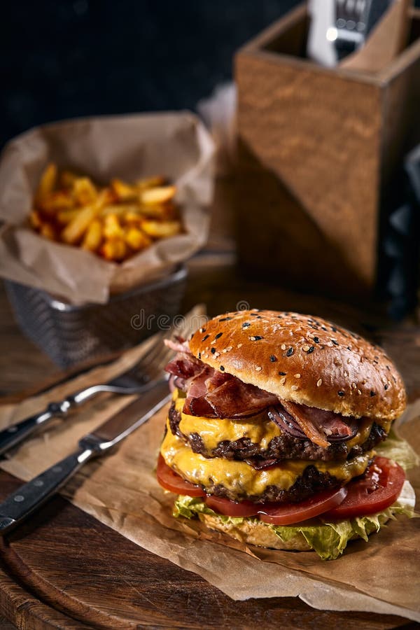 Sesame bun cheeseburger με ζουμερές μπιφτέκι και φρέσκα συστατικά σαλάτας σερβίρονται με τηγανιτές πατάτες σε τσαλακωμένο καφέ στοκ εικόνα με δικαίωμα ελεύθερης χρήσης