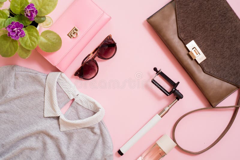 Set clothes, a purse and a bag, a comb and sunglasses, a self-stick and eau de toilette. Flowers are next to a pink background. Fa