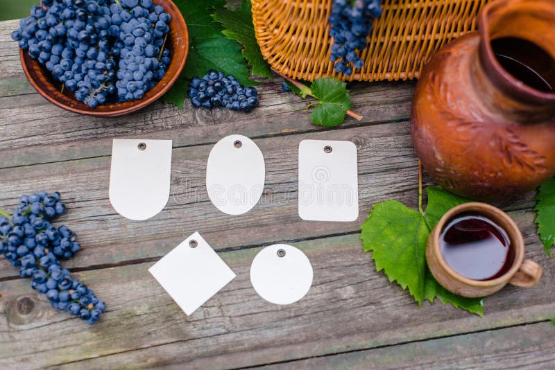 Set of different tags lay beside basket,bowl with grapes, jar and cup with wine on rustic wood. Wine making background. stock photo