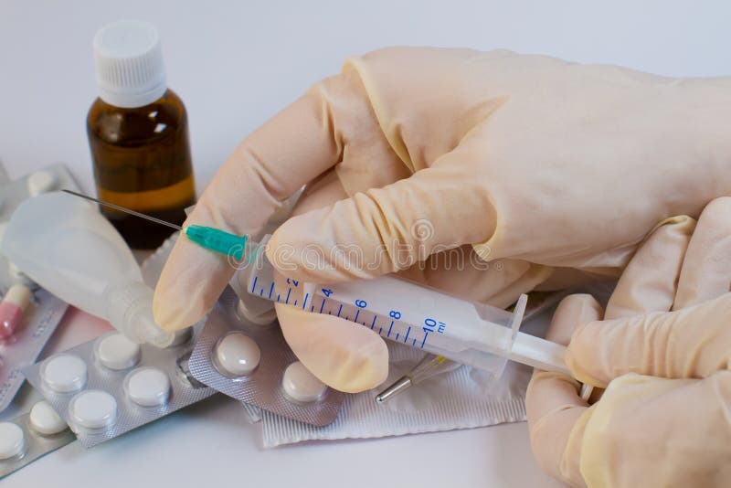 Syringe in the hands of a doctor. Tablets and glass bottles in the background.Set of drugs.