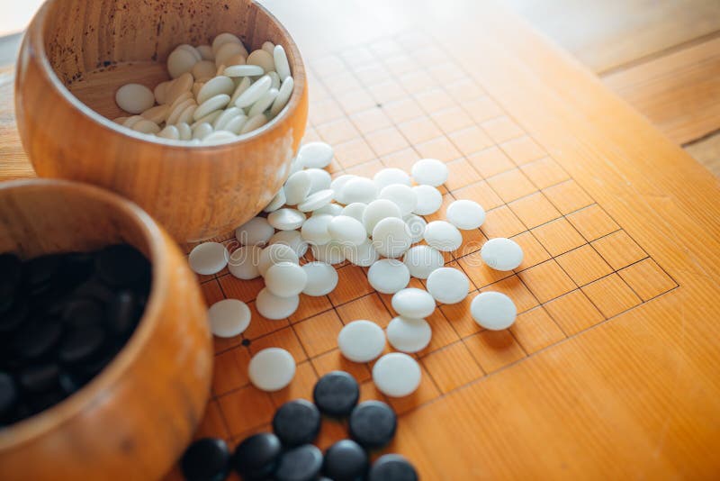 A Set of Go or Igo Game Stones in the Wooden Bowls on the Grid Table