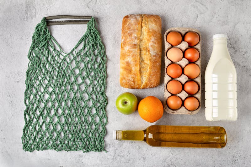 Set of grocery items with healthy food in eco string bag milk, eggs, oil, bread and fruits flat lay on gray background