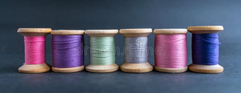 Set of pastel colors thread for sewing on a black background. Set of threads on bobbins retro style. Line coils with threads. Vintage accessories for sewing on the table. Multicolor spools of thread