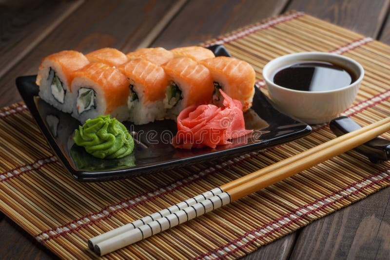 Set of Philadelphia Sushi Roll set on ceramic plate with wasabi, ginger, soy sauce and chopsticks