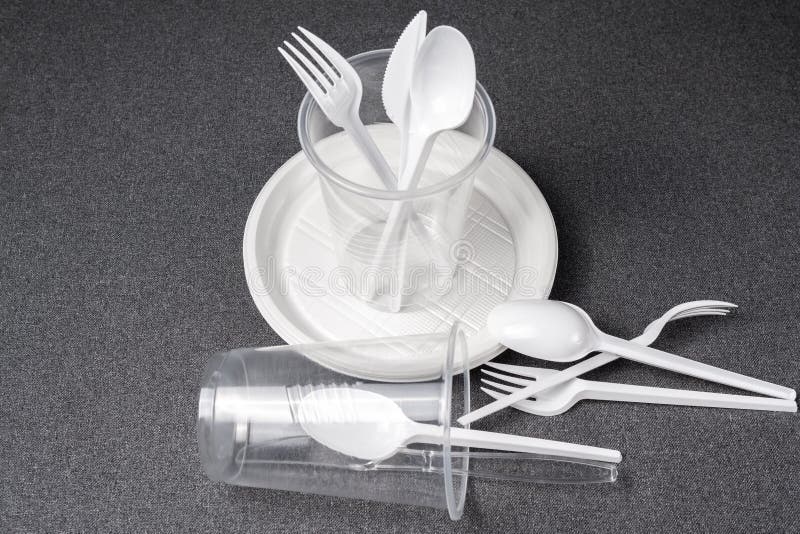 A set of plastic utensils. Plastic cups, plates, forks, spoons and plastic containers on a gray background. Against plastic stock photography