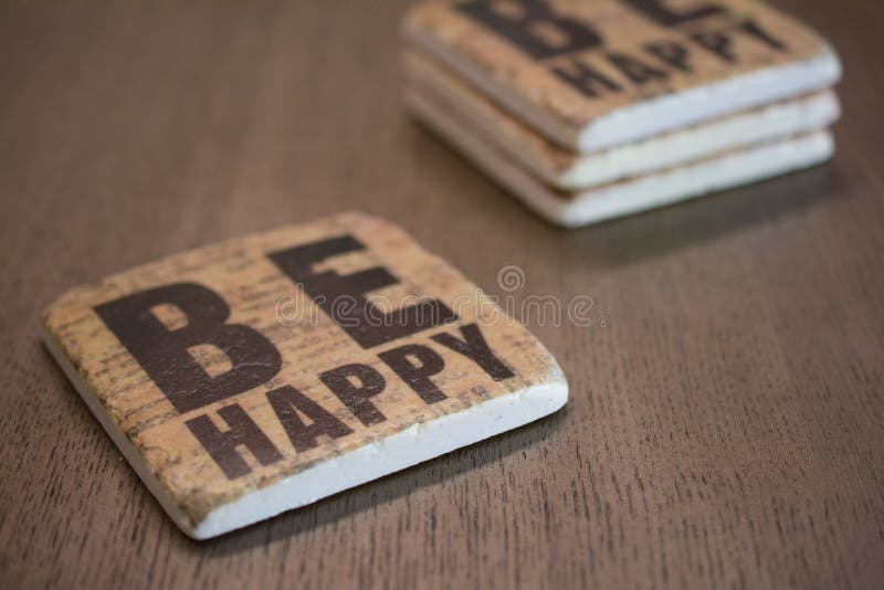 A set of stone coasters stacked on a wooden table surface reading Be Happy. A set of stone coasters stacked on a wooden table reading Be Happy royalty free stock photos A set of stone coasters stacked on a wooden table surface reading Be Happy. A set of stone coasters stacked on a wooden table reading Be Happy royalty free stock photos