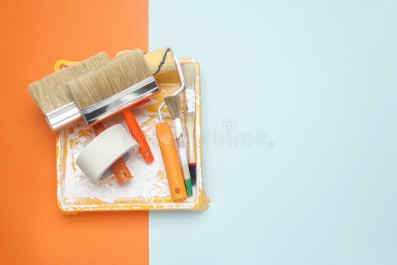 Set of tools for painting: paint brushes, masking tape, paint roller on orange and blue background. Painter work tool