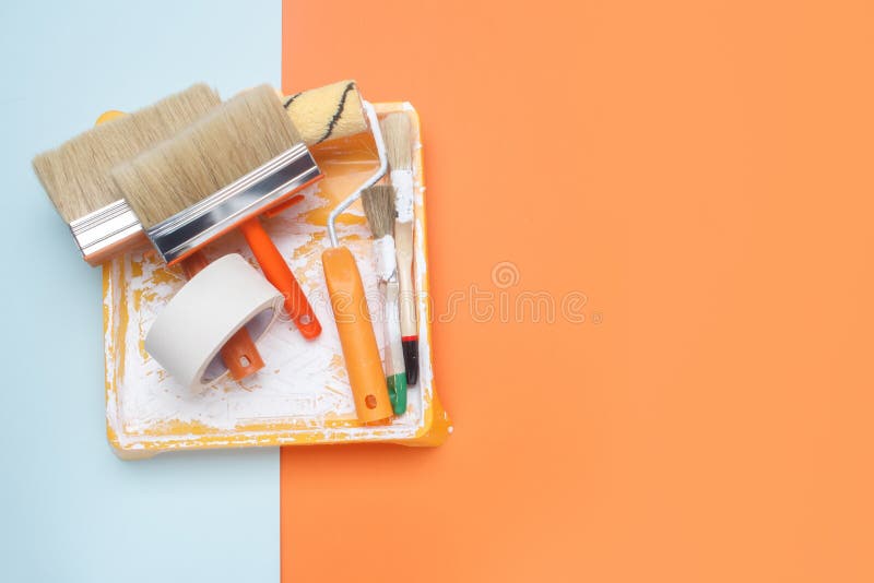 Set of tools for painting: paint brushes, masking tape, paint roller on orange and blue background. Painter work tool