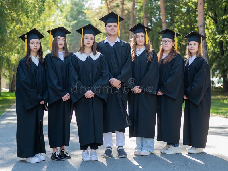 Seven graduates in robes stand in a row outdoors. Seven graduates in robes stand in a row outdoors
