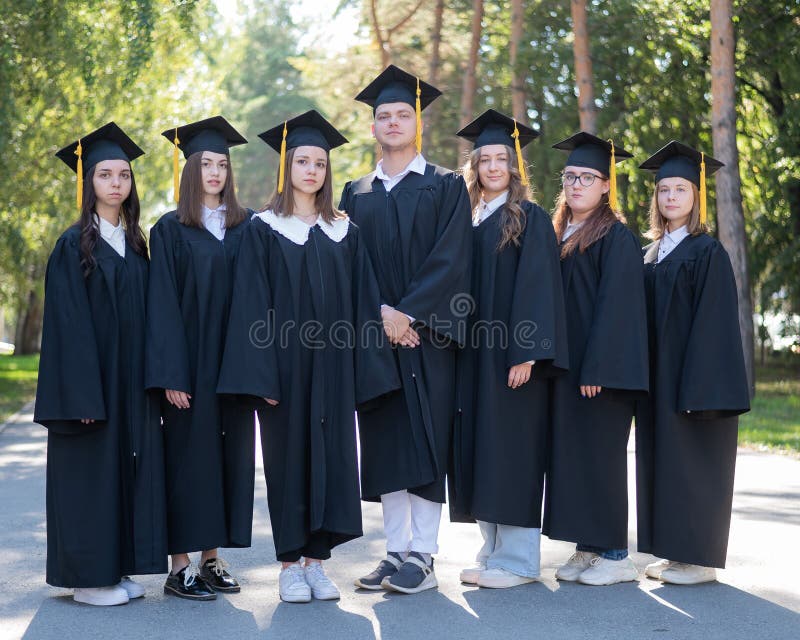 Seven graduates in robes stand in a row outdoors. Seven graduates in robes stand in a row outdoors