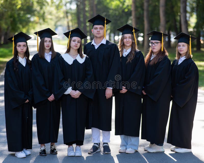 Seven graduates in robes stand in a row outdoors. Seven graduates in robes stand in a row outdoors