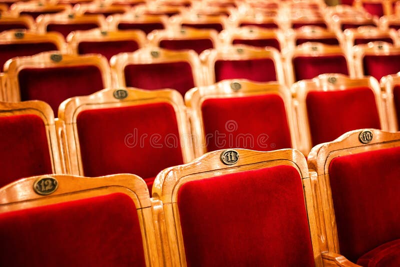 Sets on an empty theatre, taken with selective focus and shallow depth of field. Empty vintage red seats with numbers, teather cha