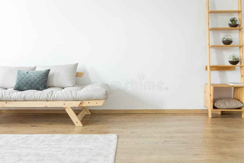 Copy space of white wall and carpet on the floor in beige living room with decoration on wooden shelves near a settee with pillows. Copy space of white wall and carpet on the floor in beige living room with decoration on wooden shelves near a settee with pillows