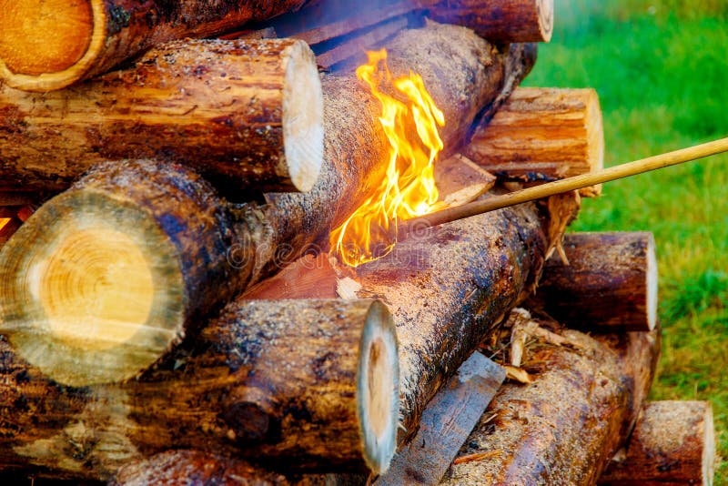 Setting Big Bonfire Made of Logs on Fire with Torch. Stock Photo