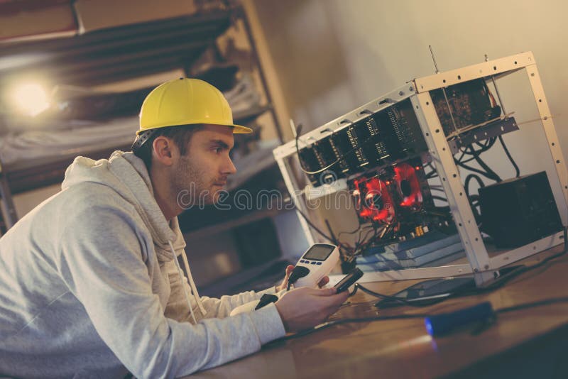 Setting up mining rig electrical energy consumption. Programmer setting up a mining rig for cryptocurrency mining, holding a wattmeter, measuring electrical energy consumption and adjusting data on smart phone app