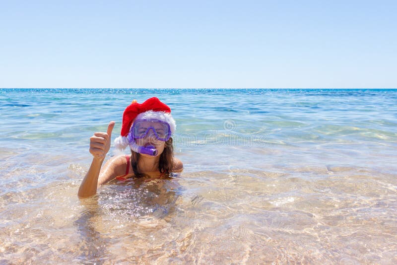 Setzen Sie die Ferienspaßfrau auf den strand, die ein Maskenrohr und einen Weihnachtshut für das Schwimmen im Ozeanwasser trägt N lizenzfreies stockbild Setzen Sie die Ferienspaßfrau auf den strand, die ein Maskenrohr und einen Weihnachtshut für das Schwimmen im Ozeanwasser trägt N lizenzfreies stockbild