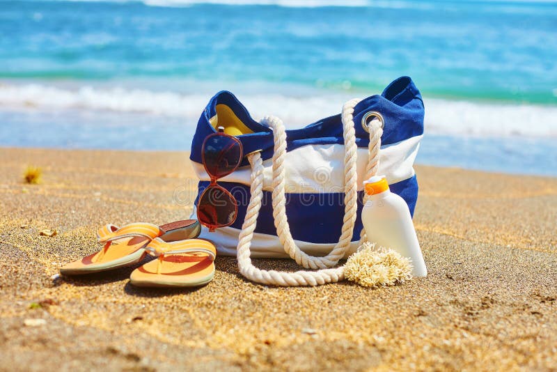 Beach bag, flip flops, sunscreen bottle and sunglasses on a Balinese beach. Beach bag, flip flops, sunscreen bottle and sunglasses on a Balinese beach