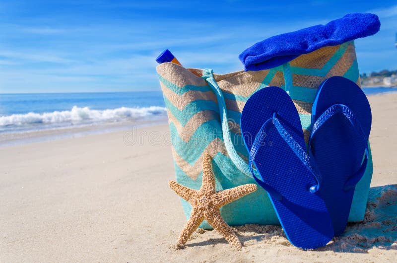 Beach bag with starfish, flip flops and towel by the ocean. Beach bag with starfish, flip flops and towel by the ocean