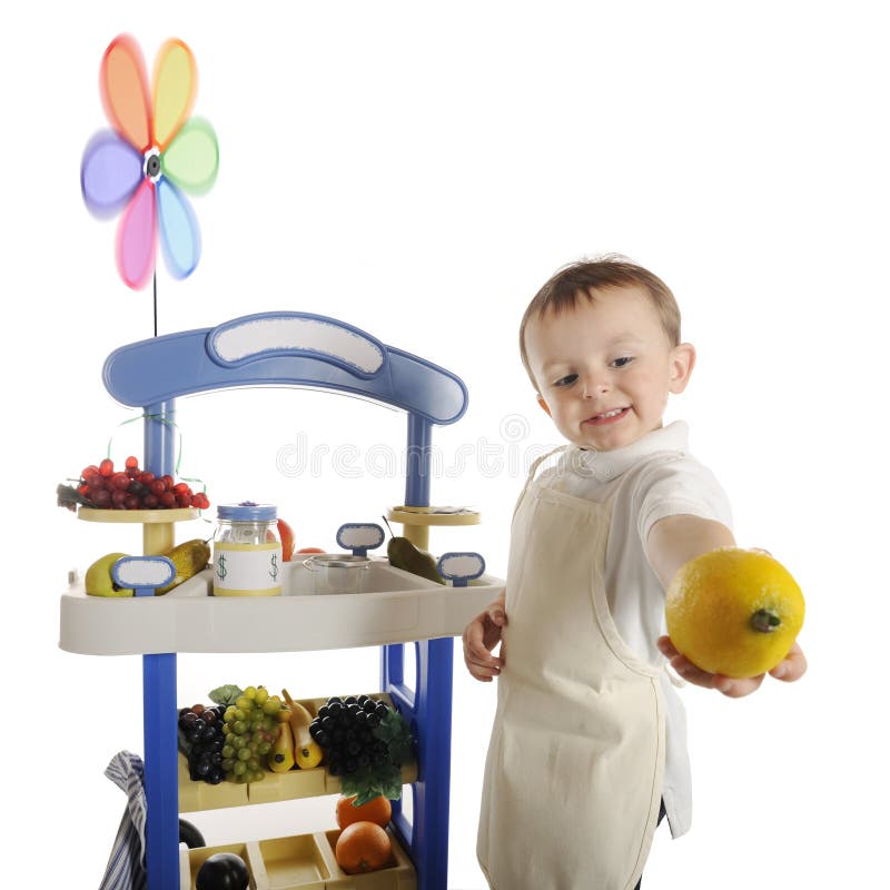 An adorable preschooler happily holding out a lemon from his fruit stand. Signs left blank for your text. Motion blur on the pinwheel. On a white background. An adorable preschooler happily holding out a lemon from his fruit stand. Signs left blank for your text. Motion blur on the pinwheel. On a white background.