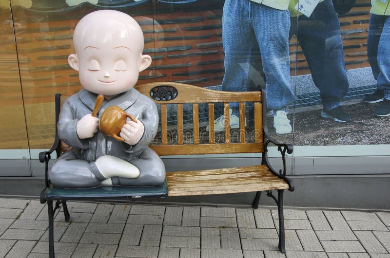 SEUL, COREIA DO SUL - 20 DE OUTUBRO DE 2019: Figura cerâmica de um monge num banco em frente à janela de uma loja em uma rua em S foto de stock royalty free SEUL, COREIA DO SUL - 20 DE OUTUBRO DE 2019: Figura cerâmica de um monge num banco em frente à janela de uma loja em uma rua em S foto de stock royalty free