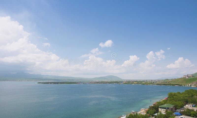 从Sevanavank修道院的看法对市的Sevan 塞凡湖、山、蓝天与云彩和天际 的臂章 库存图片