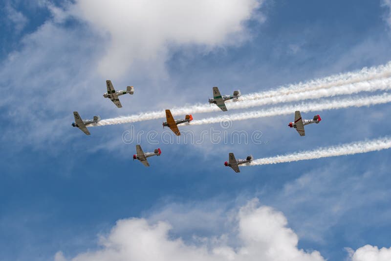 EDEN PRAIRIE, MN - JULY 16, 2016: AT6 Texan planes fly overhead against cloudy sky with smoke trails at air show. The AT6 Texan was primarily used as trainer aircraft during and after World War II. EDEN PRAIRIE, MN - JULY 16, 2016: AT6 Texan planes fly overhead against cloudy sky with smoke trails at air show. The AT6 Texan was primarily used as trainer aircraft during and after World War II.