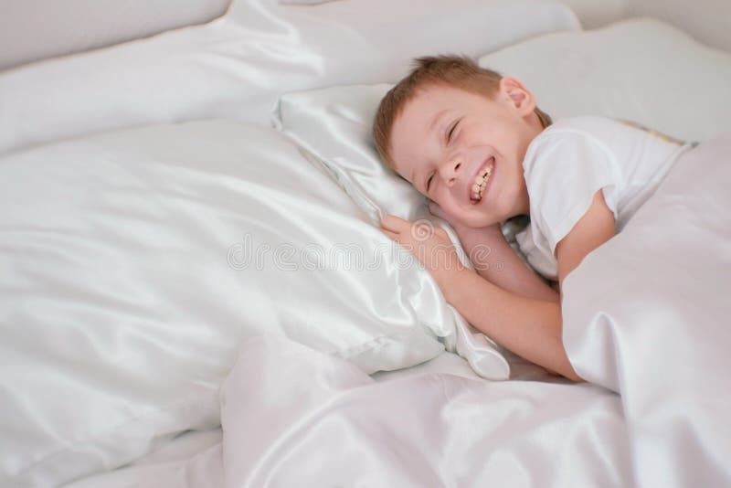 Sevenyearold Boy Just Woke Up and Laughs while Lying in Bed. Stock