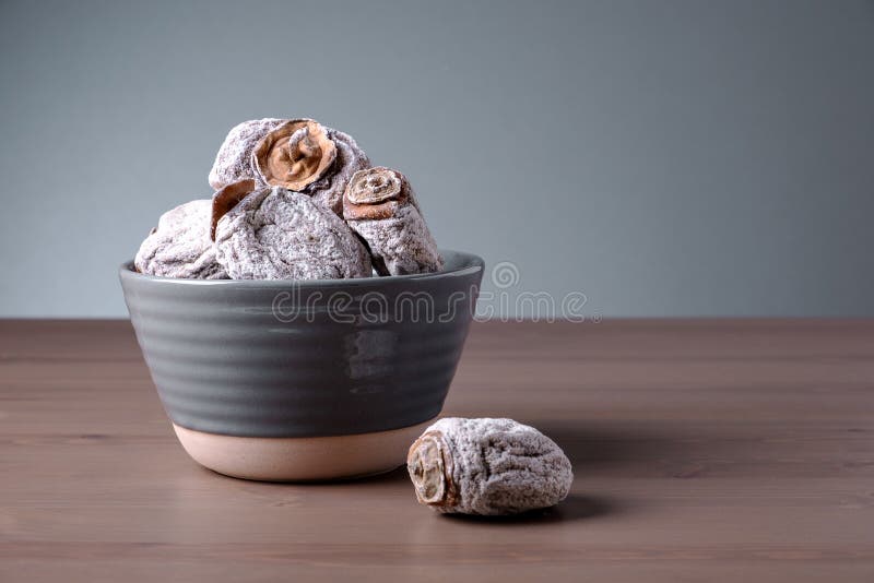 Several dried persimmons in ceramic bowl. This is useful product for diseases of endocrine and digestive systems, blood vessels, beriberi and anemia. Selective focus.