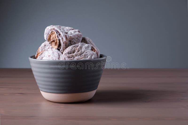 Several dried persimmons in ceramic bowl. This is useful product for diseases of endocrine and digestive systems, blood vessels, beriberi and anemia. Selective focus.