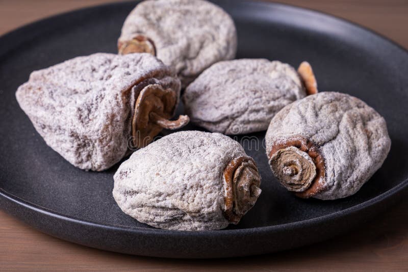 Several dried persimmons in a ceramic plate. This is a useful product for diseases of the endocrine and digestive systems, blood vessels, beriberi and anemia. Selective focus. Copy space, close-up.