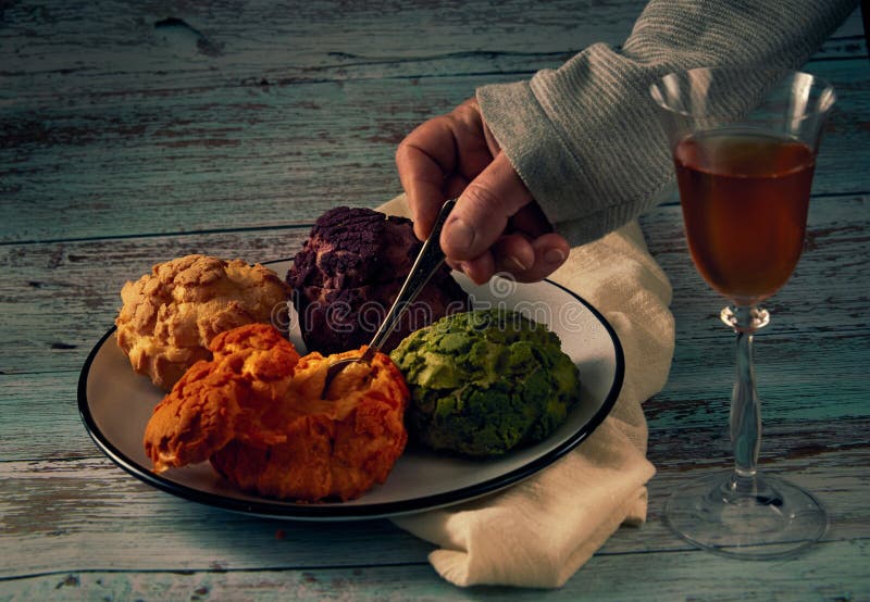 Several multi-colored profiteroles of cakes on a ceramic plate, a hand with a teaspoon and a glass of misted white wine on a stock images
