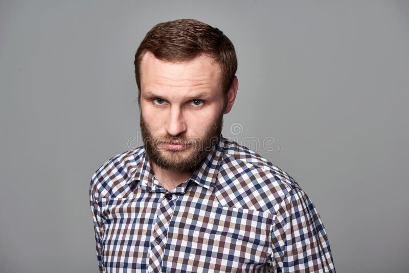 Severe bearded man in checkered shirt. Portrait of severe bearded man in checkered shirt standing on gray background staring at camera royalty free stock image Severe bearded man in checkered shirt. Portrait of severe bearded man in checkered shirt standing on gray background staring at camera royalty free stock image