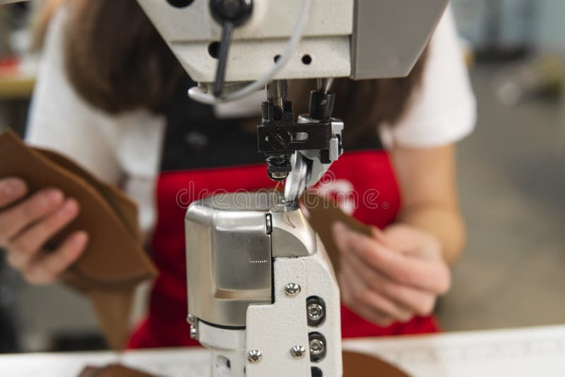 Sewing machine in a leather workshop in action with hands working on a leather details for shoes. Women`s hands with. Material, closeup.