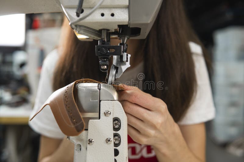 Sewing machine in a leather workshop in action with hands working on a leather details for shoes. Women`s hands with. Craft, factory.