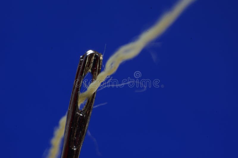 Sewing Needle with a Yellow Thread Passing through the Groove on a Blue