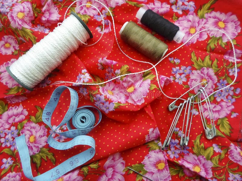 Sewing tools: colored sewing threads, centimeter ribbons and colored pins on a red background close-upвц stock photo Sewing tools: colored sewing threads, centimeter ribbons and colored pins on a red background close-upвц stock photo