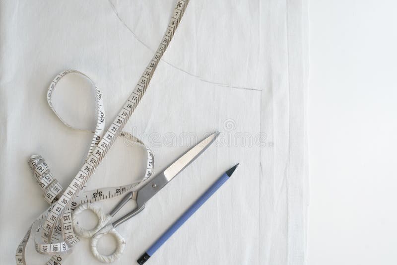 Sewing workplace, top view. Pencil, measuring tape, scissors and white cloth with sketch on the table royalty free stock image