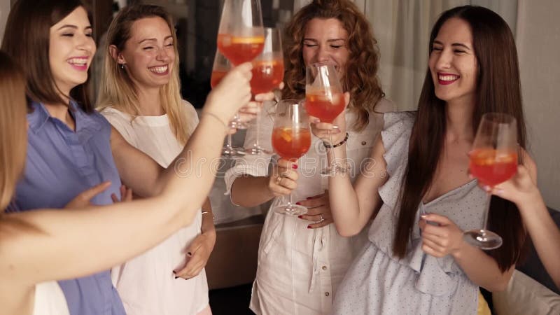 Sex flickor som står i en nära cirkel och meddelar Fira som dricker drycker från exponeringsglas jubel inomhus