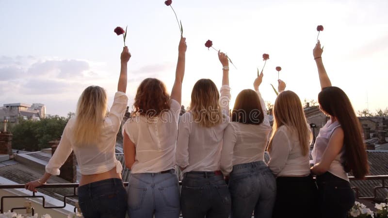 Sex förföriska unga kvinnor står på en terrass i rad från deras baksida Bärande tillfällig kläder, vita skjortor och