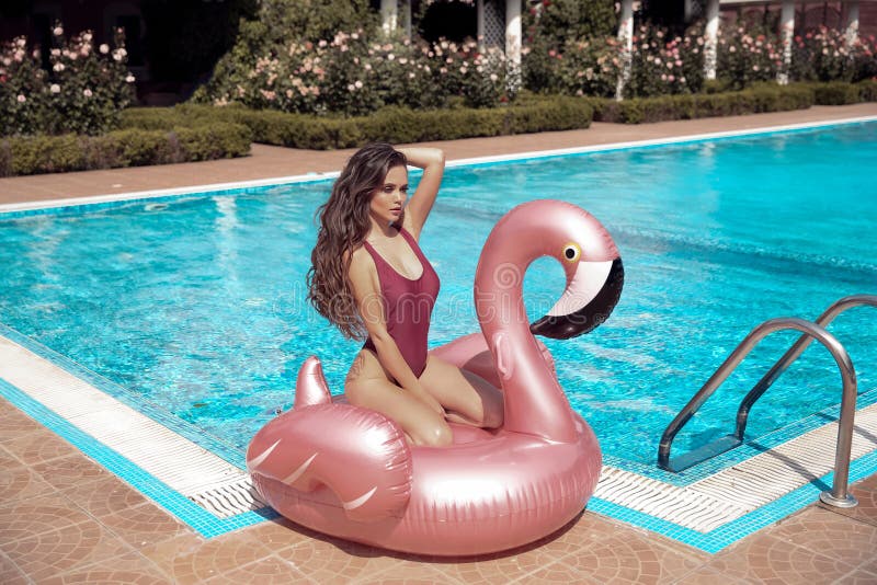 Sexig bikiniflickamodell som tycker om på den uppblåsbara jätte- rosa madrassen för flamingopölflöte i modeswimwear Attraktiv bru arkivbilder Sexig bikiniflickamodell som tycker om på den uppblåsbara jätte- rosa madrassen för flamingopölflöte i modeswimwear Attraktiv bru arkivbilder