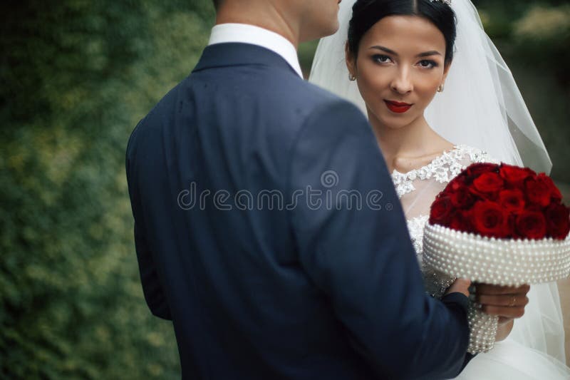 Sexig emotionell brunettbrud som kramar brudgum- och innehavbuketten royaltyfri bild Sexig emotionell brunettbrud som kramar brudgum- och innehavbuketten royaltyfri bild
