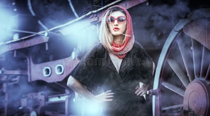 attractive girl with red head scarf and sun glasses posing on the platform in front of a vintage train. Woman vintage