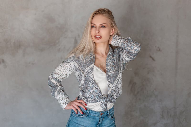 Sexy attractive young woman a blonde in a fashionable shirt with a pattern in a trendy t-shirt in stylish jeans in the studio