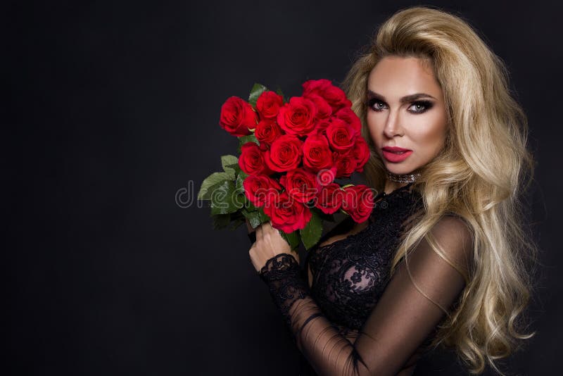 beautiful blond model in elegant dress holding a bouquet of red roses. Valentines`s gift on a black background