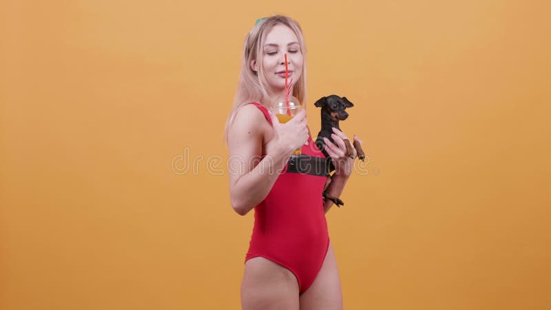 Sexy blonde girl in one piece red swimsuit with a cocktail in one hand and a dog in another